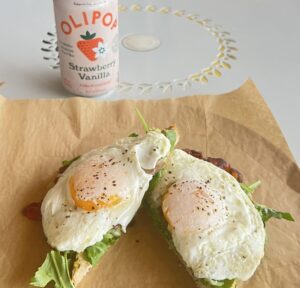 An Avocado Toast with Over Easy eggs, paired with a Strawberry Vanilla Olipop from Original ChopShop