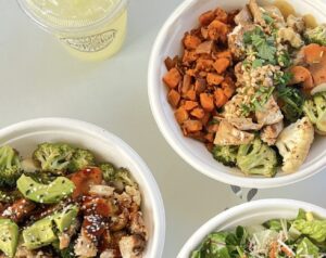 A Thai Coconut Protein Bowl and Teriyaki Chicken Protein Bowl positioned on a table next to a freshly squeezed lemonade