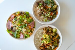 A Italian Salad, Teriyaki Chicken Protein Bowl, and Sweet Soy Sesame Steak Protein Bowl on a table from Original ChopShop